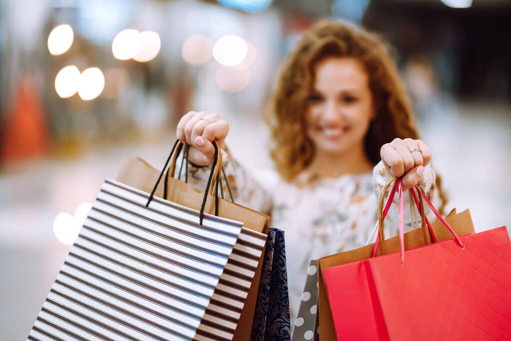 女性の手にショッピングバッグ。ショッピングバッグを持つ若い女性がモールを歩いている。春の買い物。消費主義、販売、購入、ライフスタイルの概念. - 写真・画像