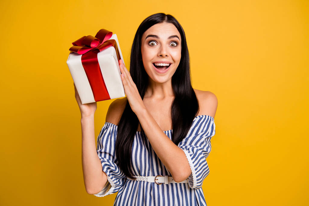 Foto de la joven encantadora excitada usar vestido a rayas adivinar regalo dentro de la caja de regalo aislado color amarillo fondo - Foto, imagen