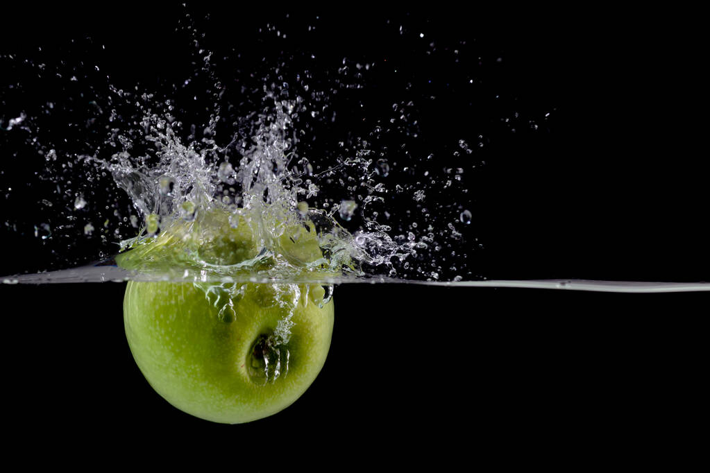 Стиглі зелене яблуко падає в чисту воду з бризками на чорному тлі
 - Фото, зображення