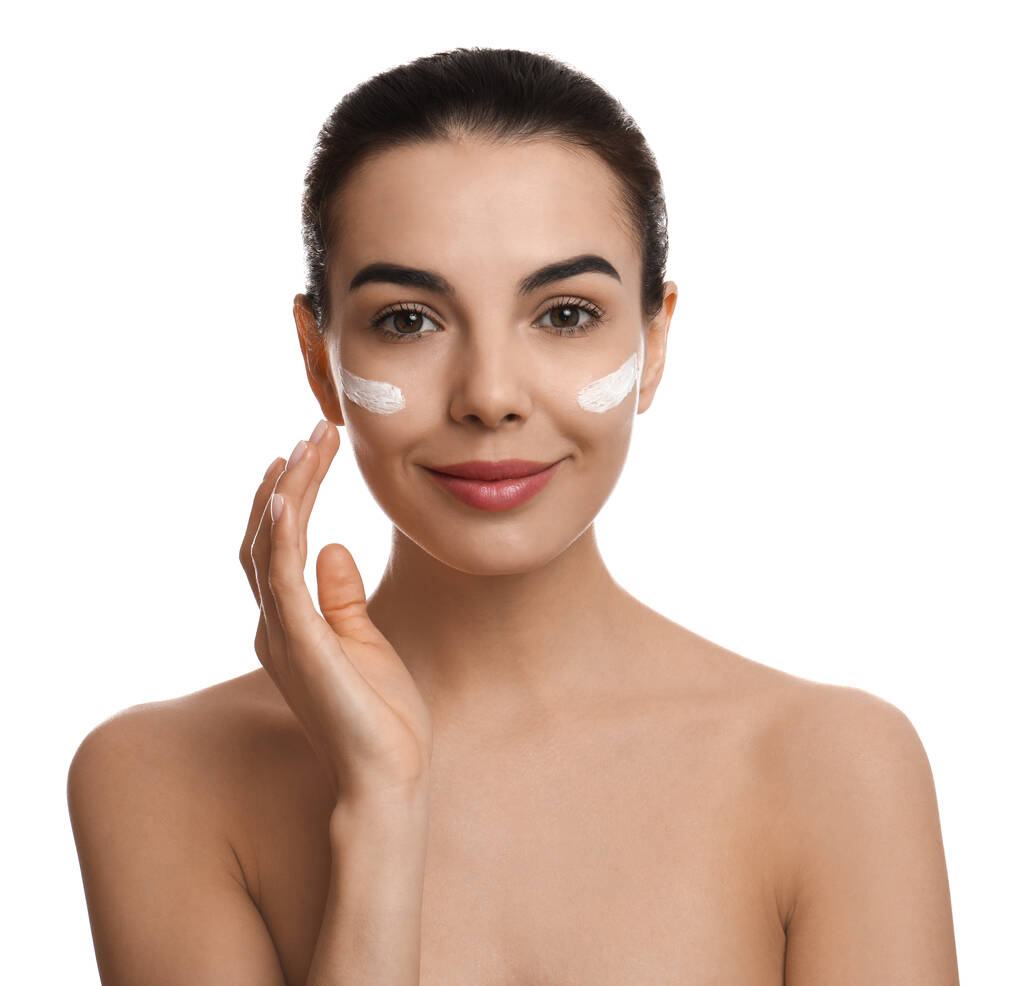 Mujer joven aplicando crema facial sobre fondo blanco - Foto, Imagen