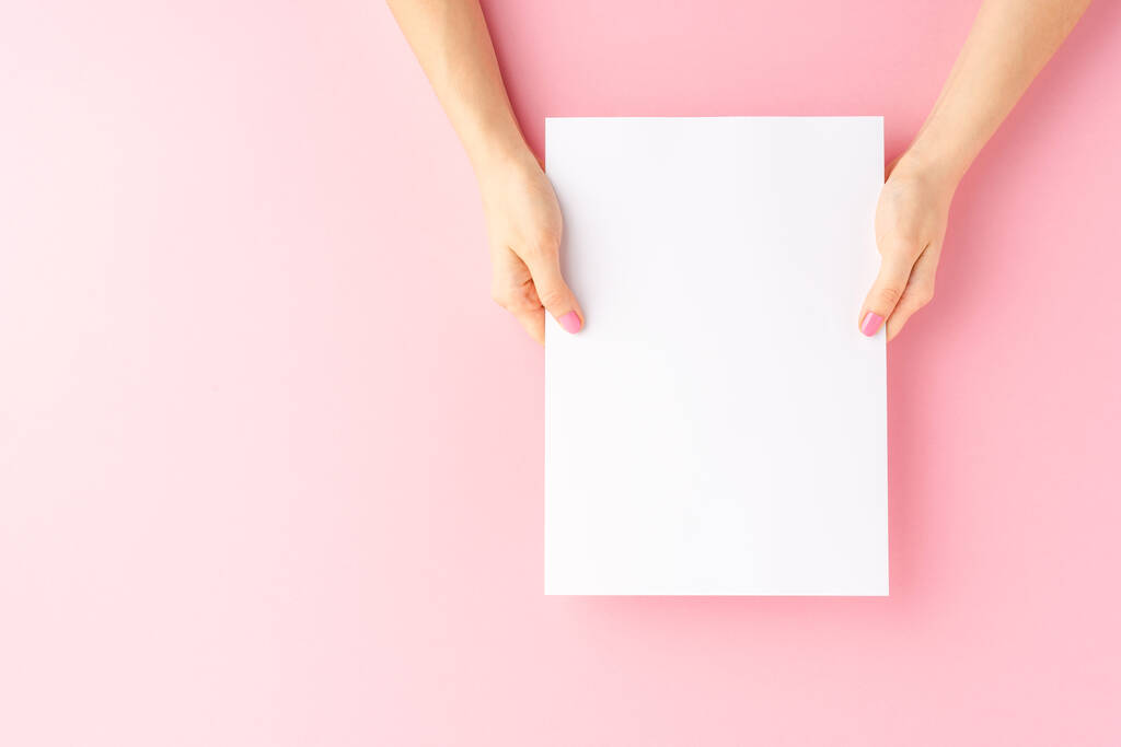 Γυναικεία χέρια κρατώντας λευκό λευκό φύλλο χαρτιού σε ροζ φόντο. Κουράγιο. - Φωτογραφία, εικόνα