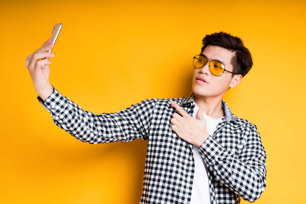 beau brutal asiatique guy dans lunettes de soleil fait un selfie sur l 'téléphone tout en tenant il dans son main - Photo, image