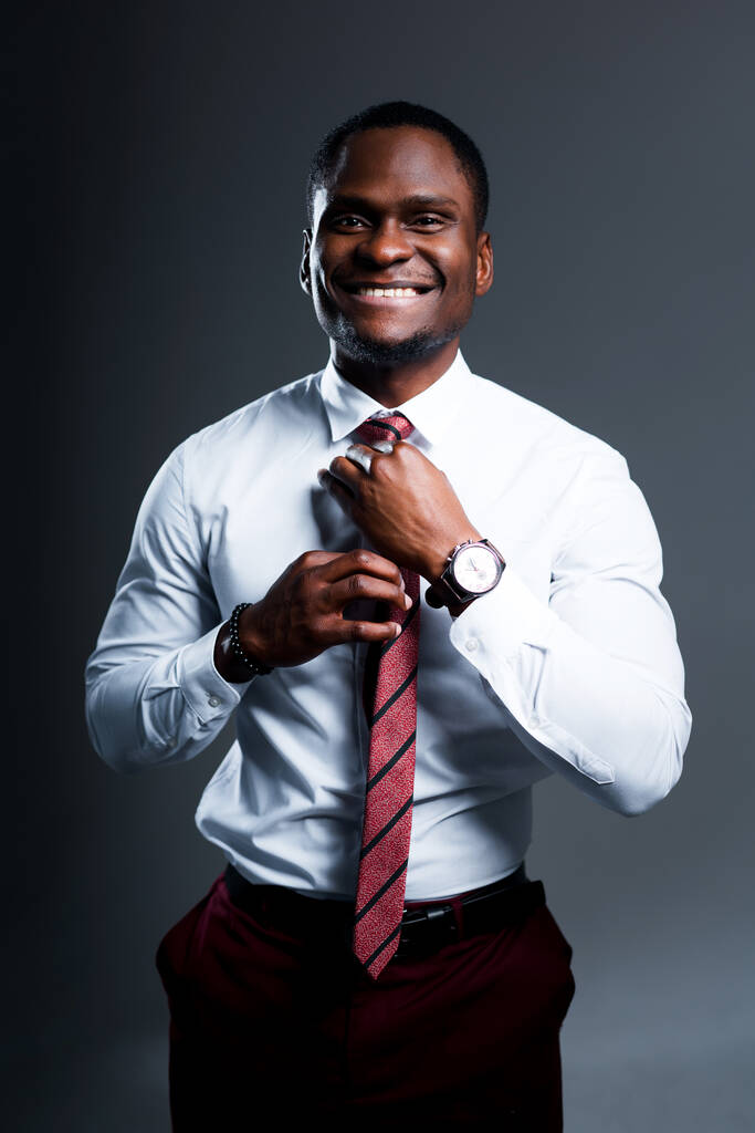 Felice uomo d'affari afroamericano in camicia bianca sorridente e legare cravatta intorno al collo - Foto, immagini