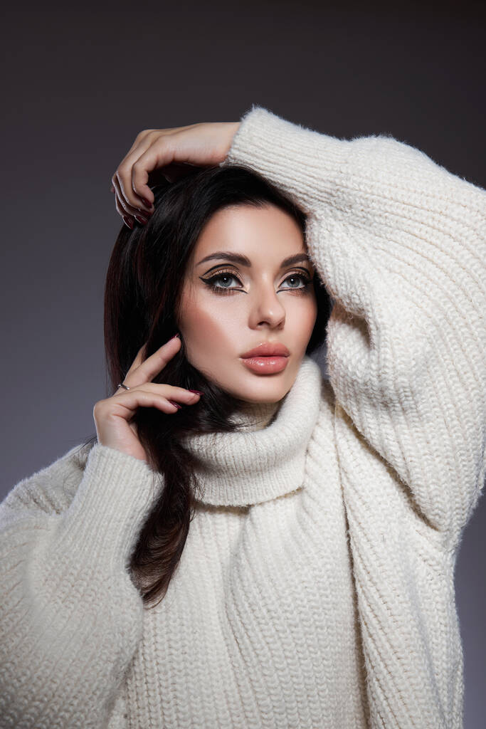 Beauty portrait of woman in white sweater, perfect evening makeup on dark background. Perfect skin without wrinkles, professional beauty makeup, long black hair - Photo, Image