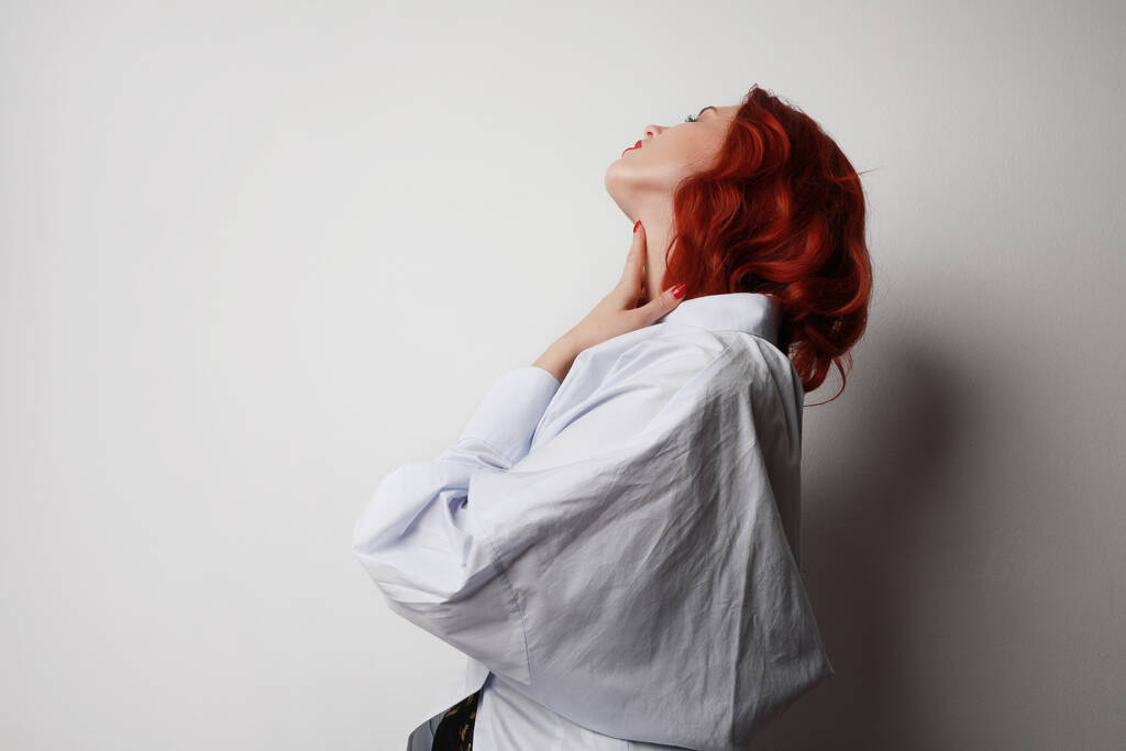 Retrato lateral de mulher jovem com cabelo vermelho posando sobre fundo cinza.  - Foto, Imagem