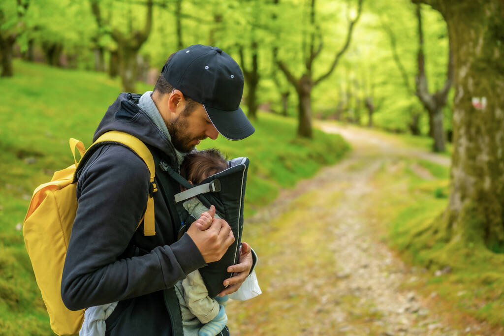 森の中のパス上のバックパックに生まれたばかりの子供と一緒に歩いて黄色のバックパックを持つ若い父親 - 写真・画像
