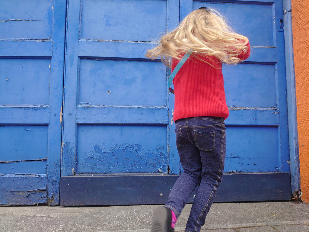 Ένα ξανθό κορίτσι που χορεύει μπροστά σε μια μπλε κατασκευή. - Φωτογραφία, εικόνα