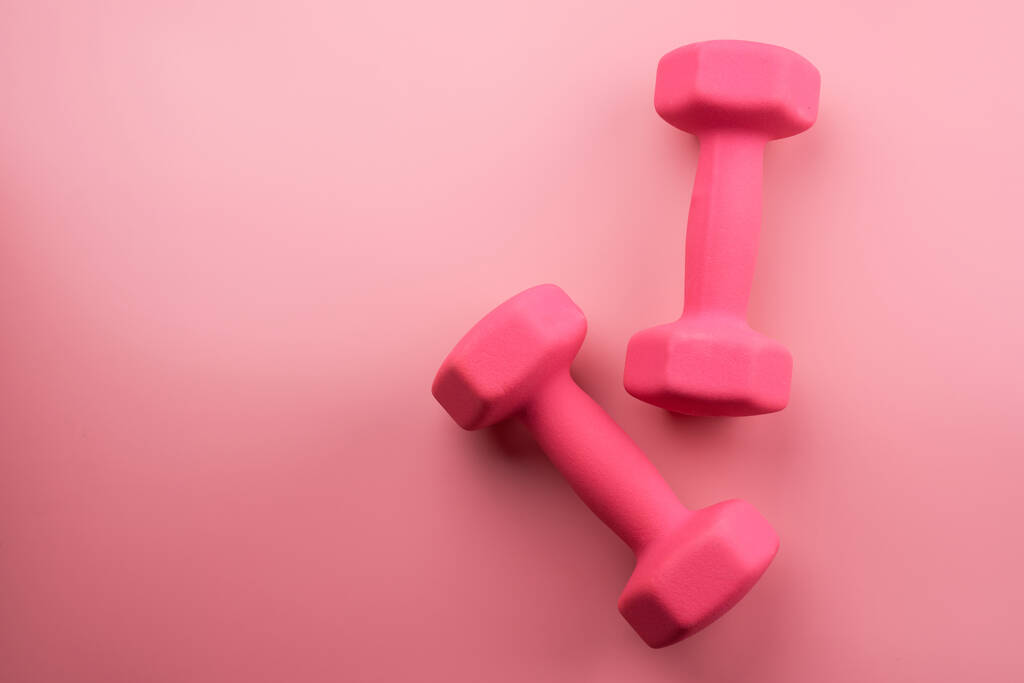 Dois halteres femininos rosa isolados no fundo rosa close-up com espaço de cópia. Conceito de aptidão, perda de peso e atividade esportiva, vista superior, flat lay - Foto, Imagem