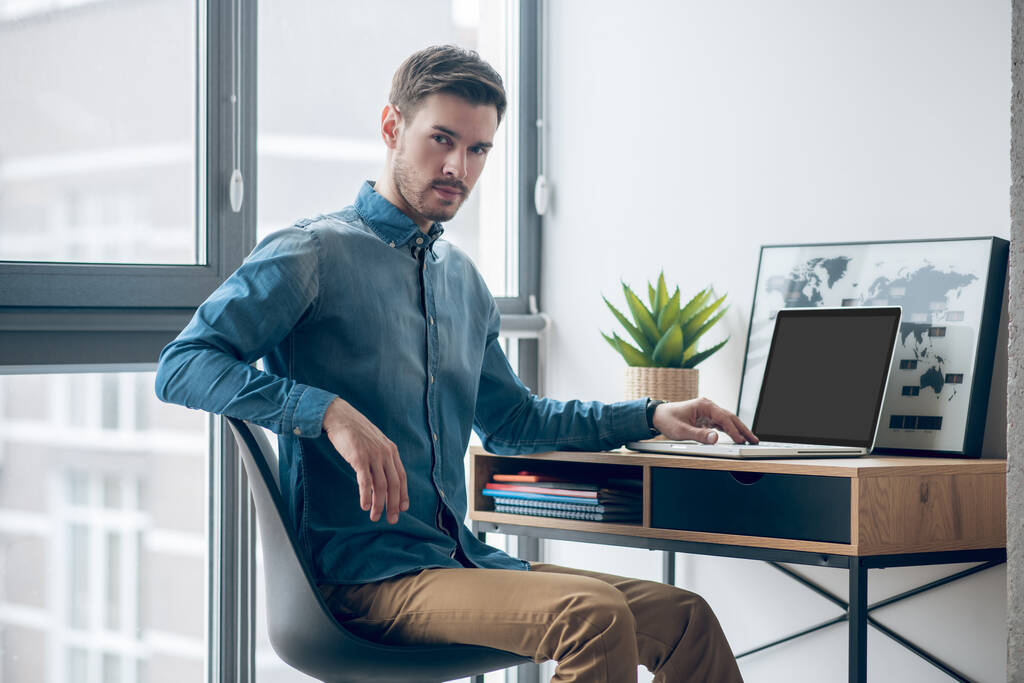 Темноволосый мужчина, сидящий за столом и работающий над ноутбуком - Фото, изображение