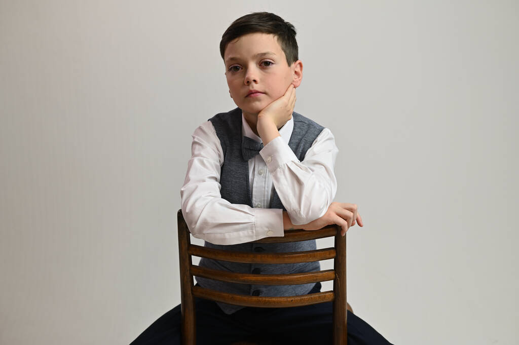 Ritratto studio foto di un ragazzo serio adolescente su uno sfondo grigio seduto su una sedia - Foto, immagini