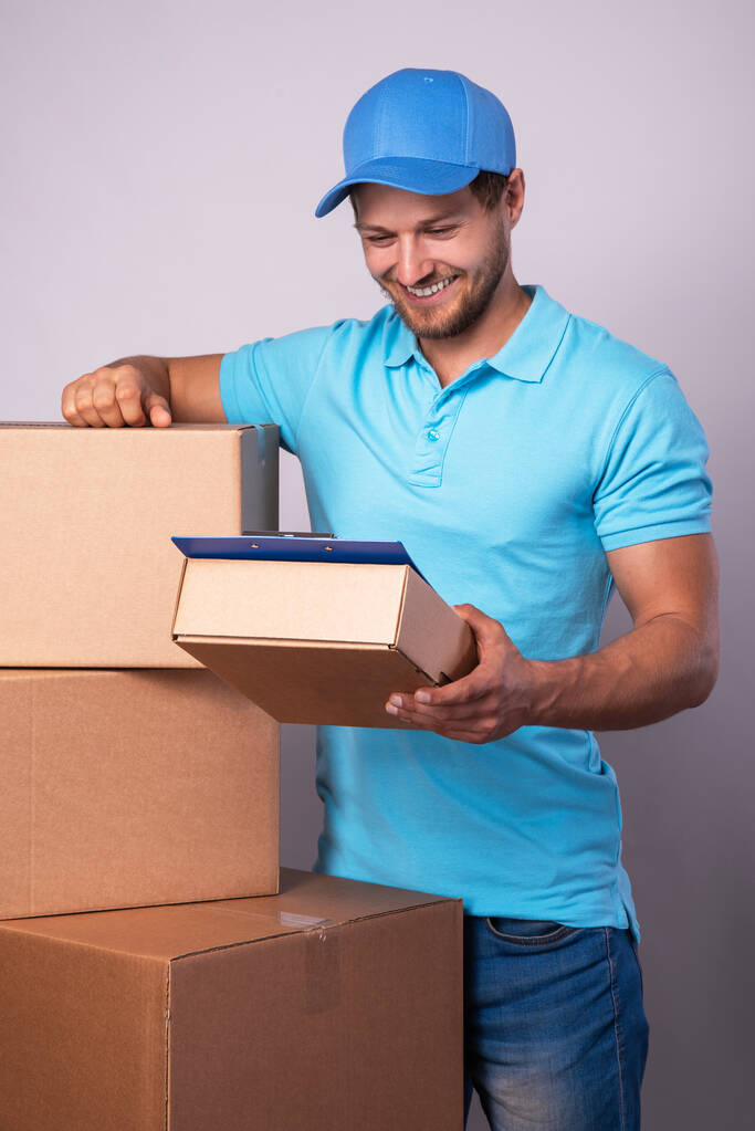 Счастливый доставщик во время работы с посылкой в картонной коробке на заднем плане - Фото, изображение
