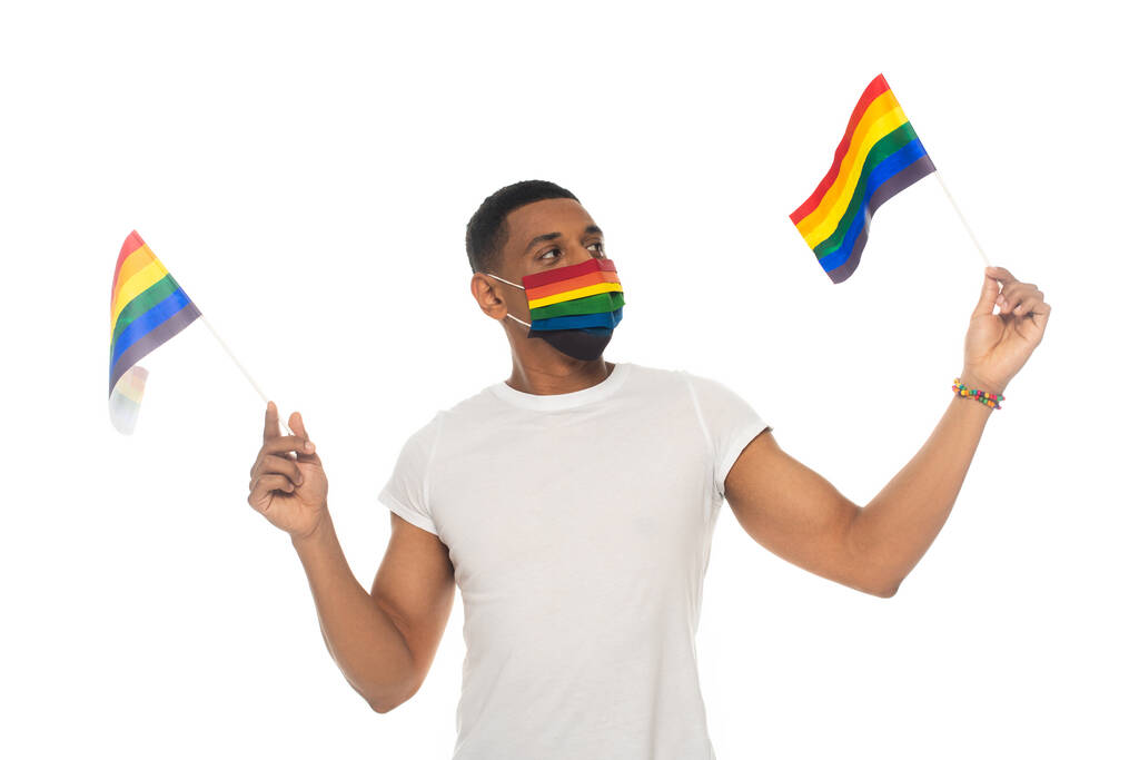 Afrikaans amerikaanse man met lgbt vlaggen terwijl het dragen van regenboog kleuren medisch masker geïsoleerd op wit - Foto, afbeelding