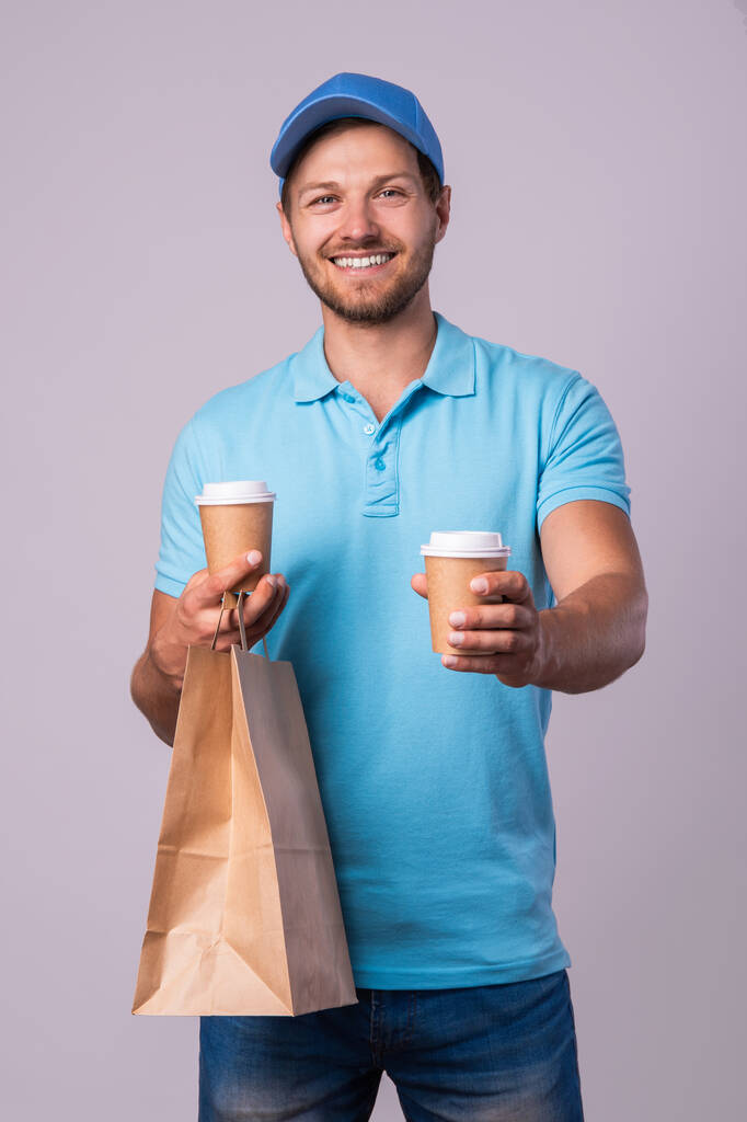 Happy delivery man with a two cups of coffee isolated on gray background - Photo, Image