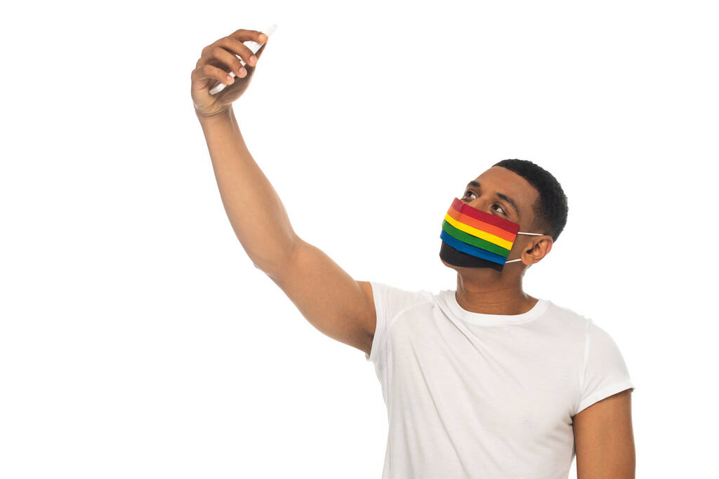 Afrikalı Amerikalı bir adam lgbt renginde tıbbi maske takıyor ve beyazlar içinde selfie çekiyor. - Fotoğraf, Görsel