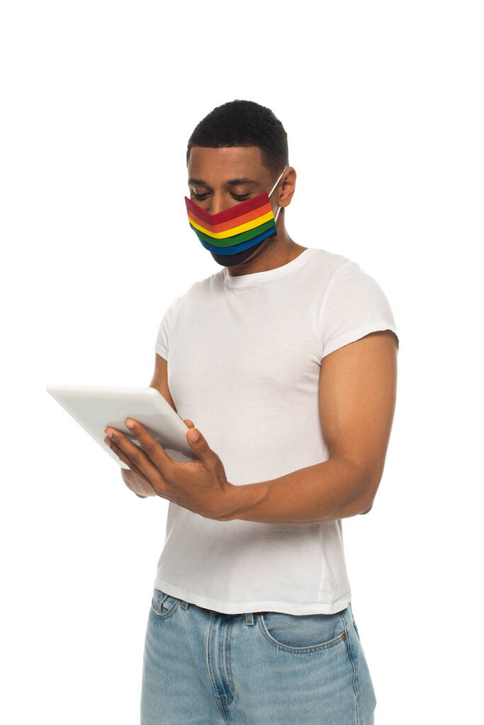 Afrykański Amerykanin noszący maskę ochronną w kolorach lgbt i wykorzystujący cyfrową tabletkę izolowaną na białym - Zdjęcie, obraz
