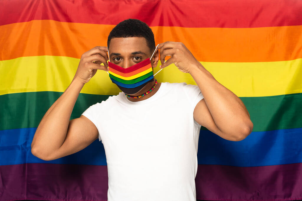 jovem homem americano africano colocando cores arco-íris máscara protetora no fundo da bandeira lgbt - Foto, Imagem