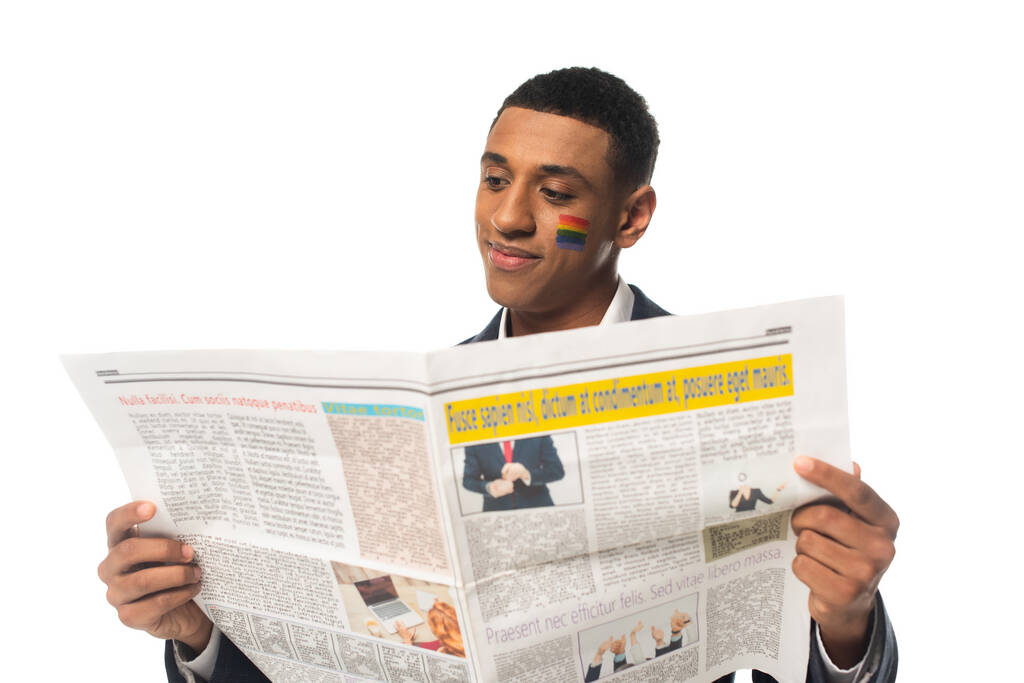веселый африканский американский бизнесмен с флагом lgbt нарисованным на лице читая газету, изолированную на белом - Фото, изображение