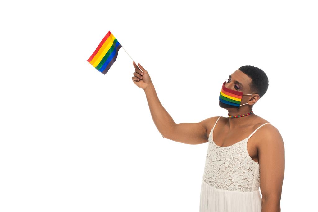 Αφροαμερικάνα τρανσέξουαλ γυναίκα, φορώντας ουράνιο τόξο χρώματα ιατρική μάσκα και κρατώντας σημαία Igbt απομονώνονται σε λευκό - Φωτογραφία, εικόνα