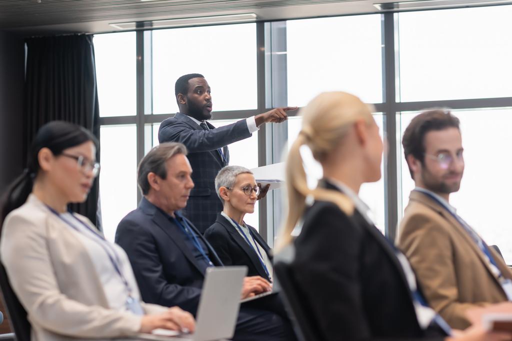 Africký americký podnikatel ukazuje prstem poblíž rozmazaných kolegů v konferenční místnosti  - Fotografie, Obrázek
