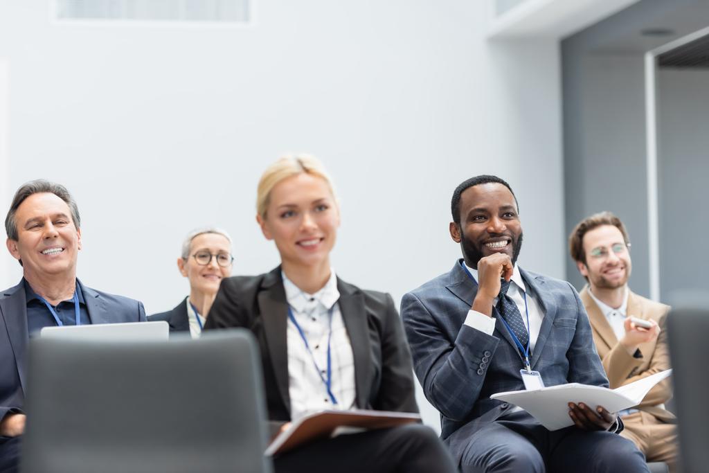 Зрелый бизнесмен с ноутбуком улыбается рядом с многонациональными коллегами в конференц-зале  - Фото, изображение