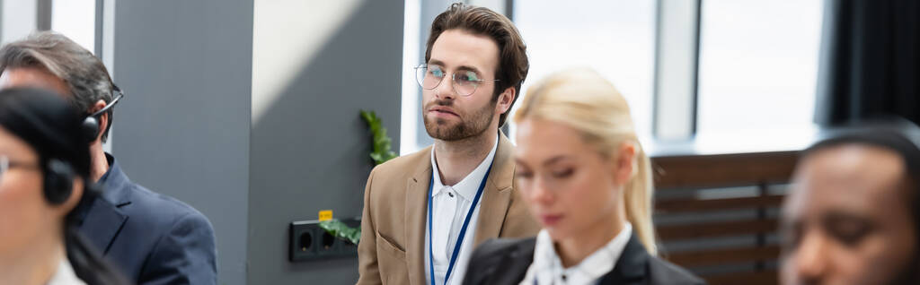 Επιχειρηματίας κοιτάζοντας μακριά κοντά σε πολυεθνικούς συναδέλφους σε ακουστικά κατά τη διάρκεια της διάσκεψης, πανό  - Φωτογραφία, εικόνα