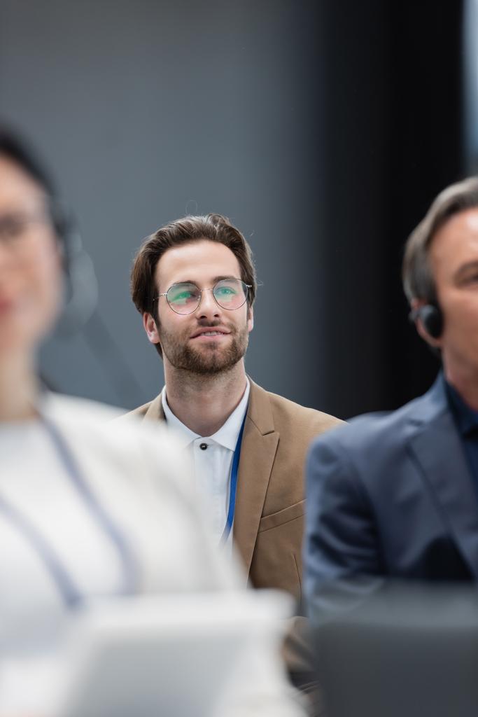 селективный фокус молодого бизнесмена в очках рядом с размытыми коллегами на семинаре - Фото, изображение