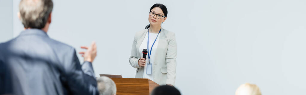 Asijský přednášející poslouchající rozmazaného podnikatele kladoucí otázky během semináře, banner - Fotografie, Obrázek