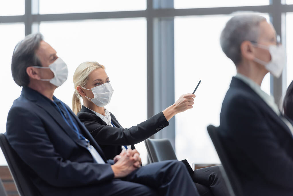 jovem empresária em máscara médica apontando com caneta perto de colegas durante o seminário - Foto, Imagem