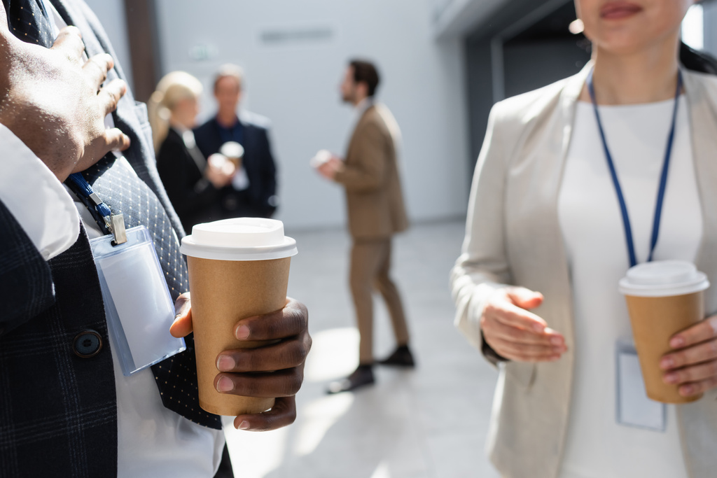 uomo d'affari afroamericano in possesso di caffè per andare vicino ai colleghi su sfondo sfocato - Foto, immagini