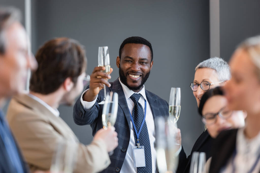 selectieve focus van Afrikaanse Amerikaanse zakenman die champagne glas in de buurt van interraciale collega 's - Foto, afbeelding