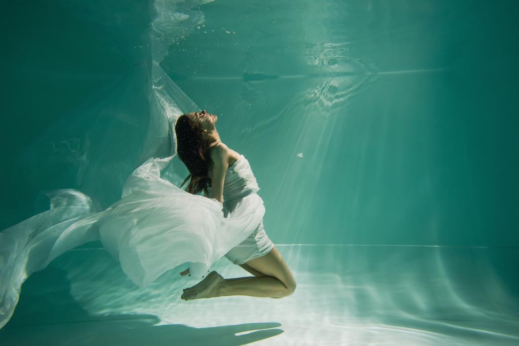 vista laterale di bruna giovane donna in abito nuoto in piscina con acqua blu  - Foto, immagini