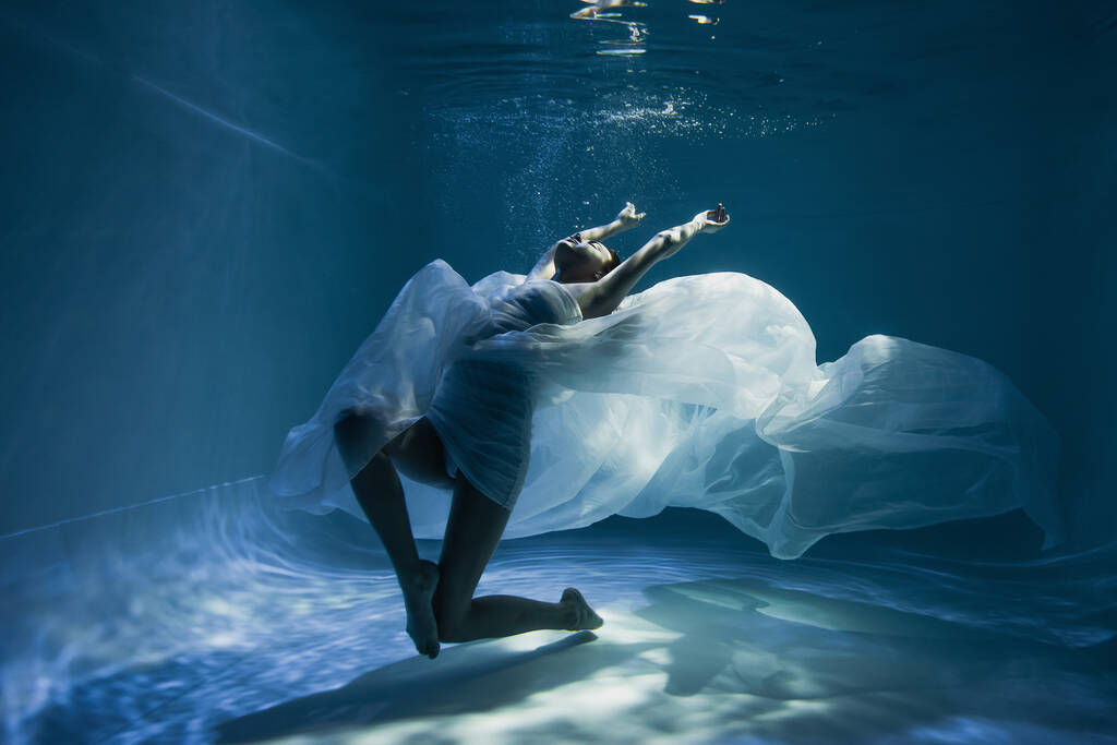 白いドレスを着た裸足の女性がプールで泳いでいて  - 写真・画像