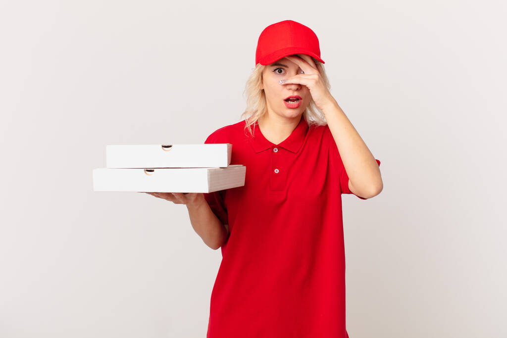 jonge mooie vrouw kijkt geschokt, bang of doodsbang, gezicht bedekken met de hand. pizza leveren concept - Foto, afbeelding
