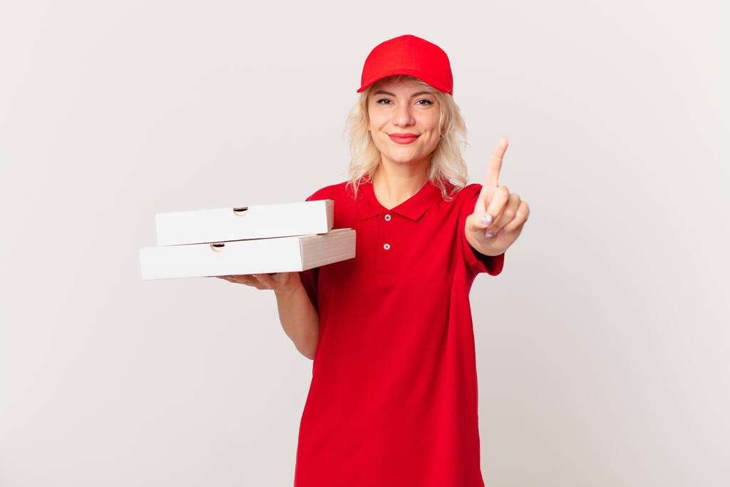 Młoda, ładna kobieta uśmiecha się i wygląda przyjaźnie, pokazując numer jeden. koncepcja dostarczania pizzy - Zdjęcie, obraz