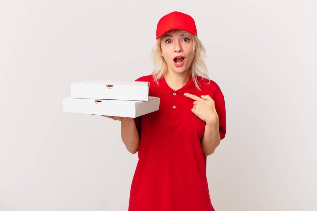 young pretty woman looking shocked and surprised with mouth wide open, pointing to self. pizza delivering concept - Foto, Imagen
