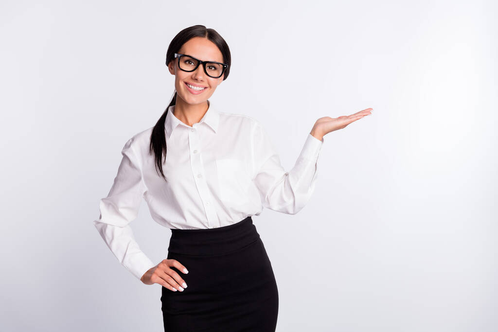 Kuva optimistinen brunette kampaus nainen pidä tyhjää tilaa kulumista silmälasit valkoinen paita eristetty harmaa väri tausta - Valokuva, kuva