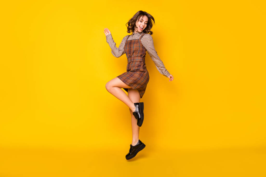Teljes hossz testméret fotó iskolás lány ugrás nevetés visel kockás egyenruha elszigetelt élénk sárga színű háttér - Fotó, kép