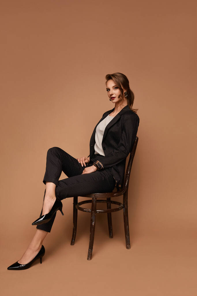 Confiant caucasien jeune femme d'affaires portant un costume gris assis sur la chaise sur fond beige, isolé avec espace de copie - Photo, image