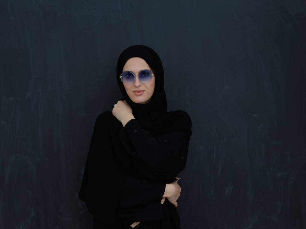 Giovani musulmani in abiti tradizionali o abaya e occhiali da sole in posa davanti alla lavagna nera. Donna araba che rappresenta lo stile di vita arabo moderno, la moda islamica e il concetto di kareem del Ramadan - Foto, immagini