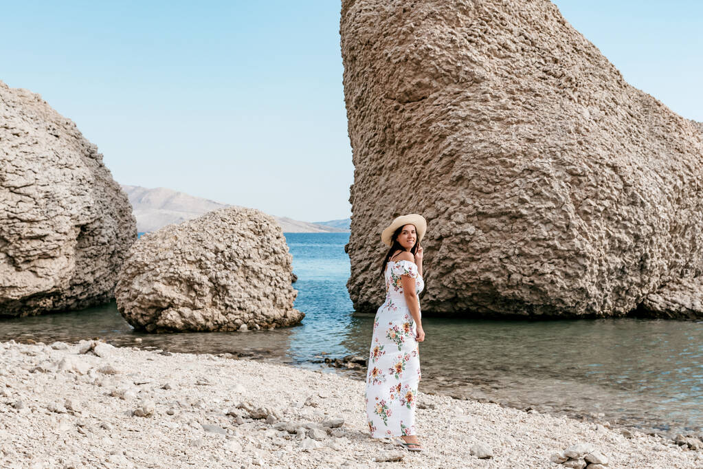 Жінка в елегантній білій літній сукні стоїть на прекрасному пляжі Беритніки з великими скелястими формами на острові Паг у Хорватії.. - Фото, зображення