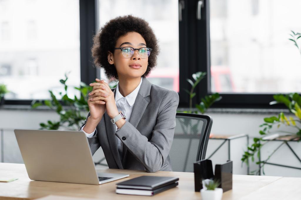 manager afroamericano in occhiali guardando lontano vicino laptop e notebook in ufficio  - Foto, immagini