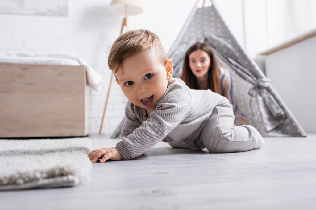 excited baby boy crawling on floor near mother on blurred background  - Photo, Image