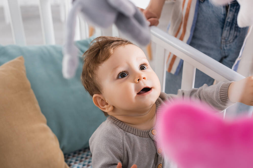 bébé garçon étonnant dans la crèche de bébé avec des jouets mous suspendus au premier plan flou - Photo, image