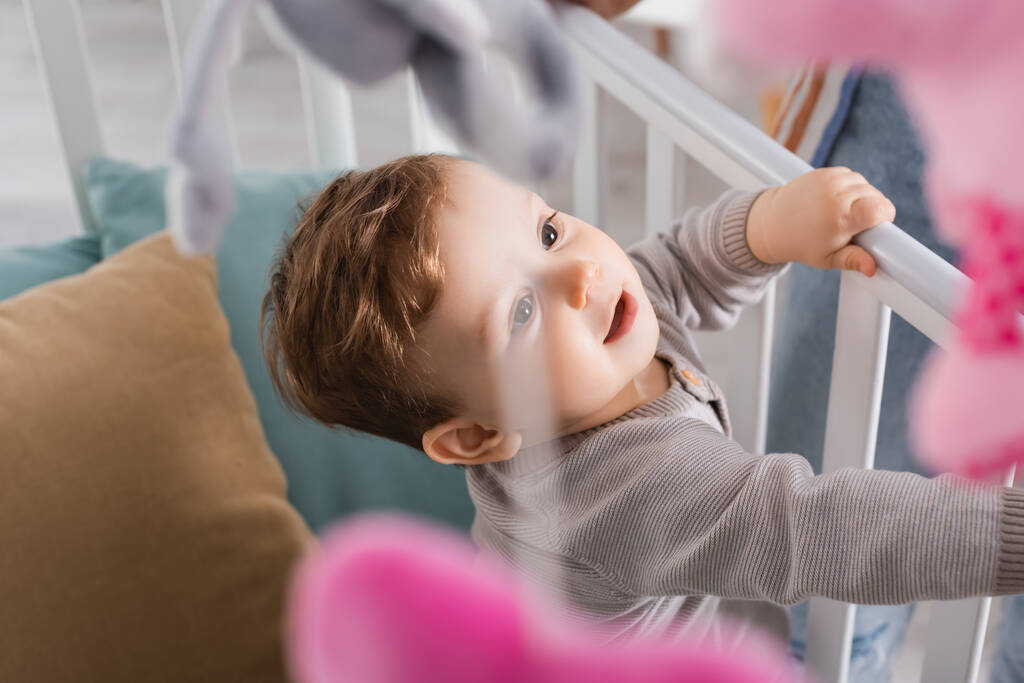 хлопчик в дитячому ліжечку з висячими м'якими іграшками на розмитому фоні
 - Фото, зображення