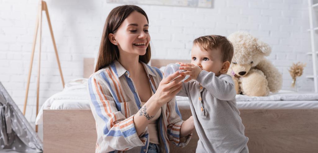 Mutlu dövmeli anne bebeğini şişeden süt ve afişle besliyor. - Fotoğraf, Görsel