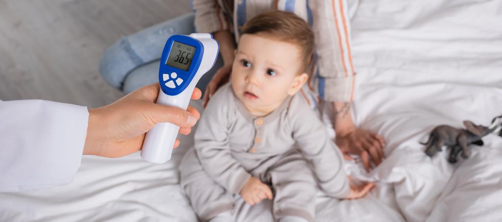 врач осматривает младенца с бесконтактным термометром рядом с матерью, баннер - Фото, изображение