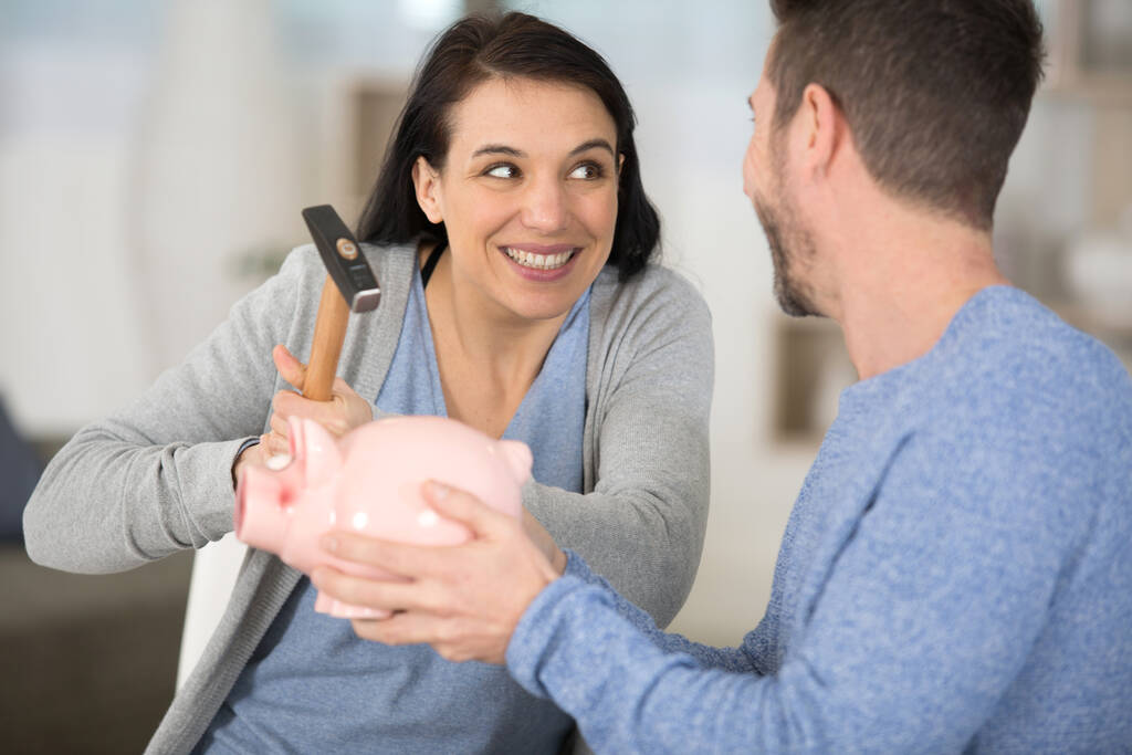 young couple breaking piggy bank with hammer at home - Photo, Image