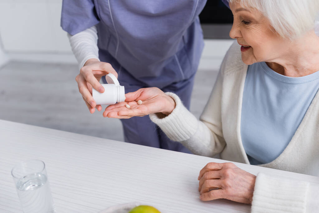 maatschappelijk werker geeft medicatie aan oudere vrouw - Foto, afbeelding