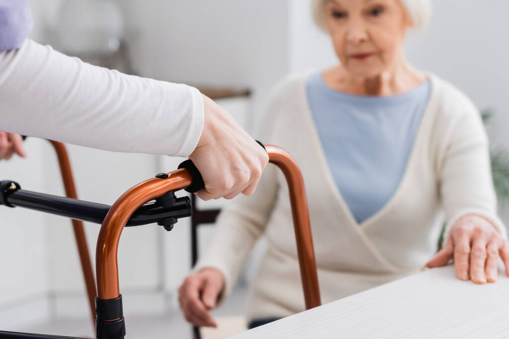 sosiaalityöntekijä, jolla on lääketieteellisiä kävelijöitä lähellä vanhempi nainen istuu hämärtyneellä taustalla - Valokuva, kuva