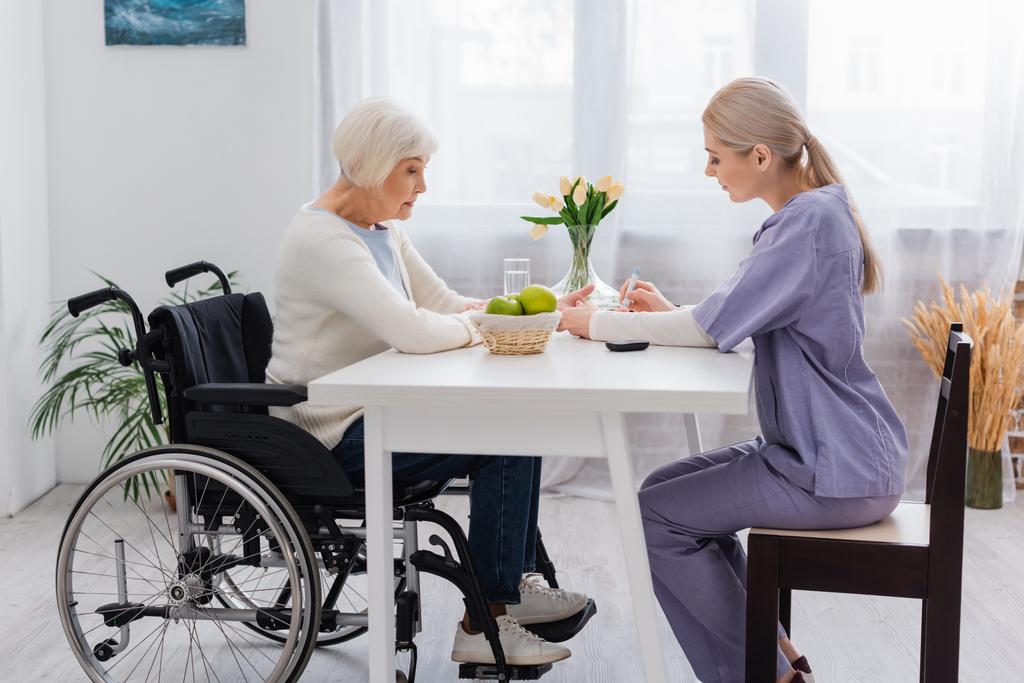 πλαϊνή όψη νοσοκόμου που κάνει ένεση ινσουλίνης σε ηλικιωμένη γυναίκα με ειδικές ανάγκες σε αναπηρικό καροτσάκι - Φωτογραφία, εικόνα